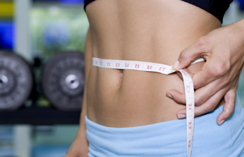 A sportswoman measuring her waist with a measurement tape.