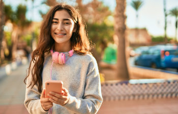 cheerful teenager with a pink phone in hand standing in the street